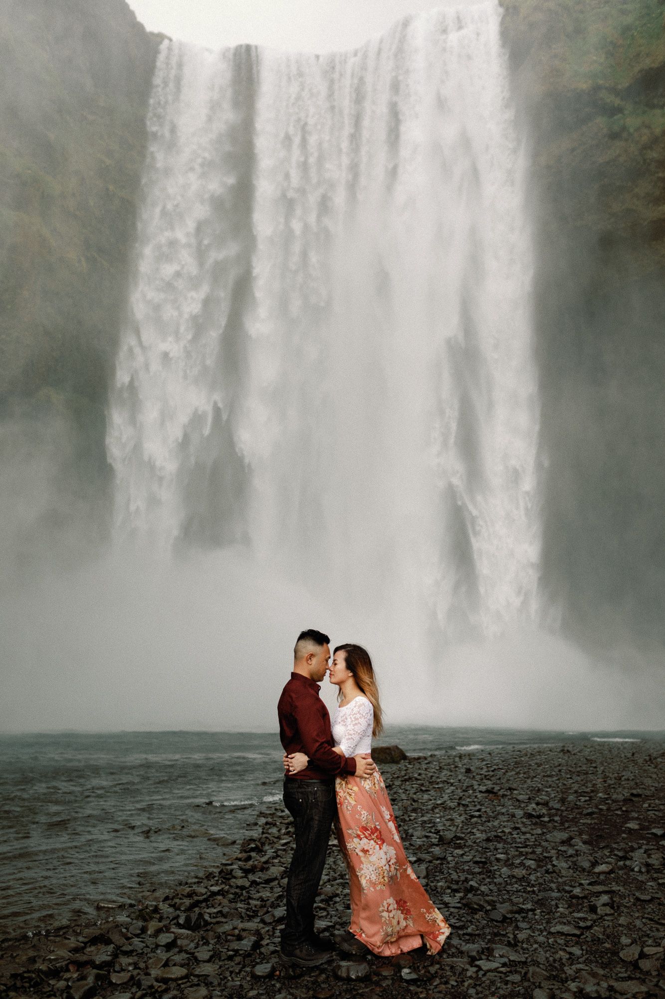 Couple sharing a romantic moment in front of the massive Skogafoss waterfall in Iceland.