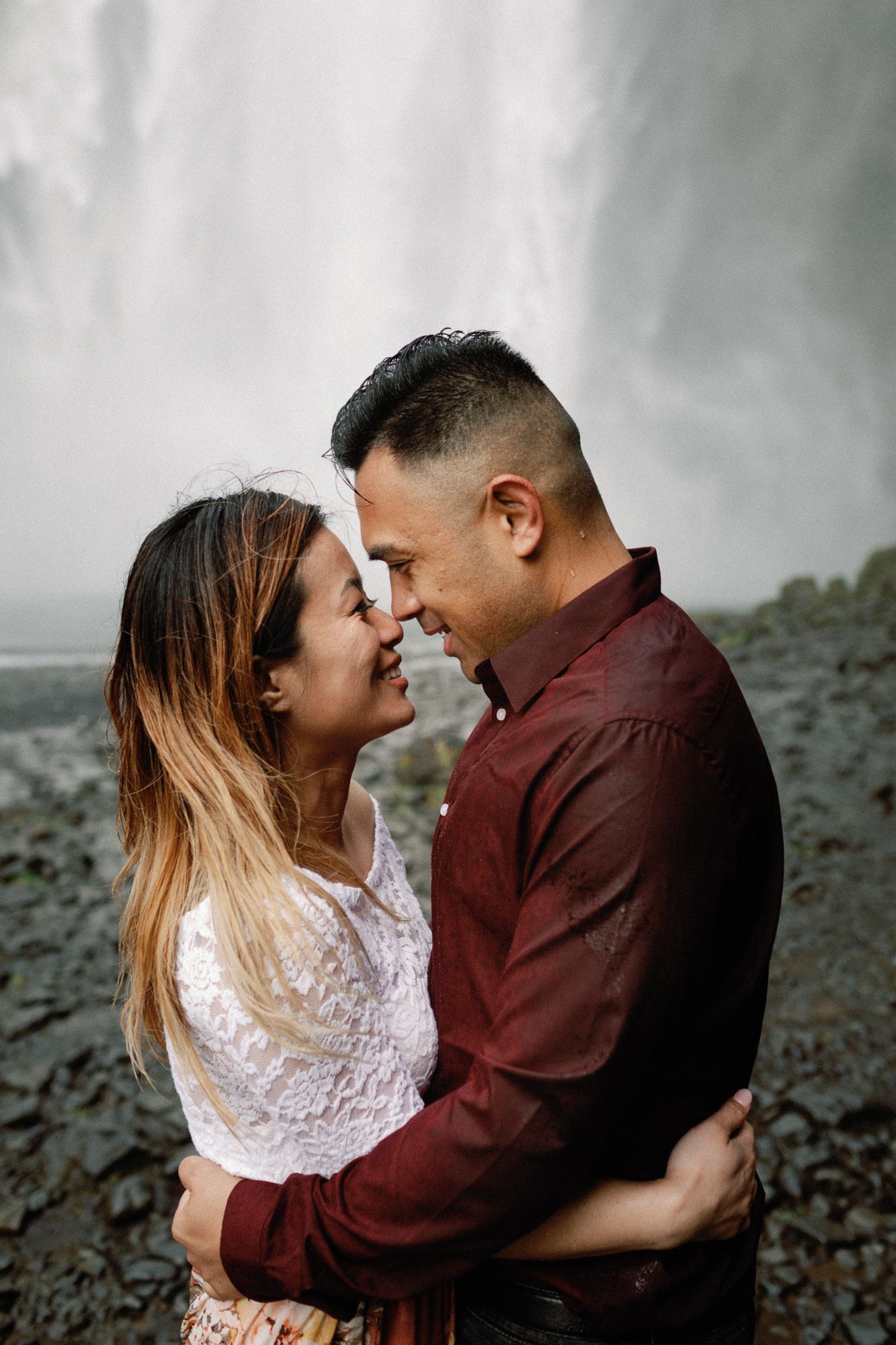 Couple smiling and touching foreheads in an intimate moment in front of Skogafoss waterfall Iceland.
