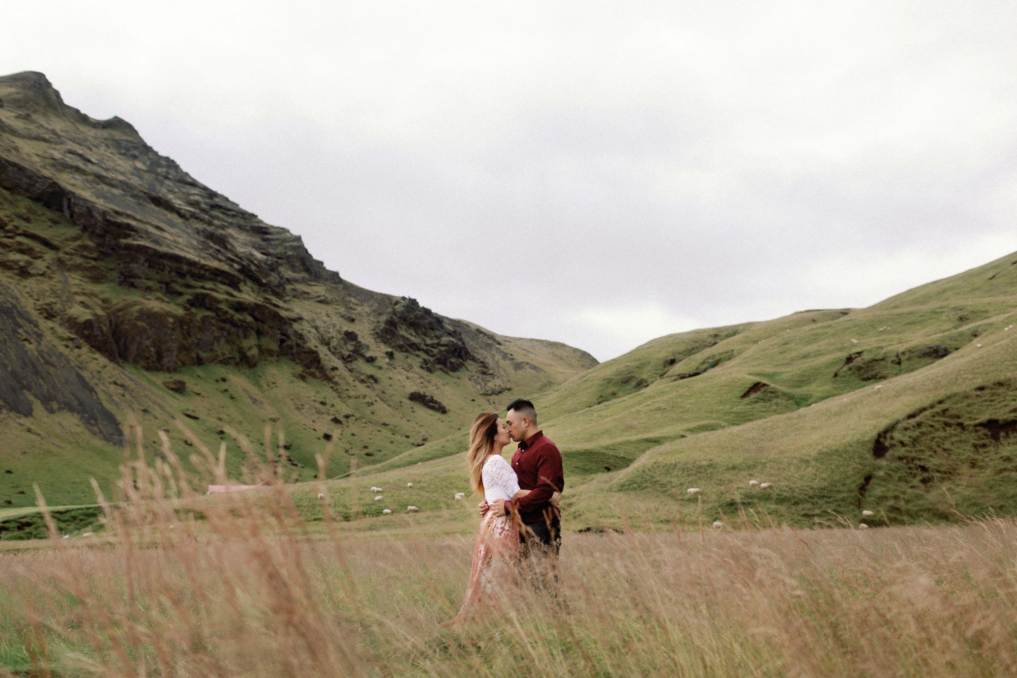 Couple embracing in a lush green valley surrounded by rolling hills in the Iceland countryside.
