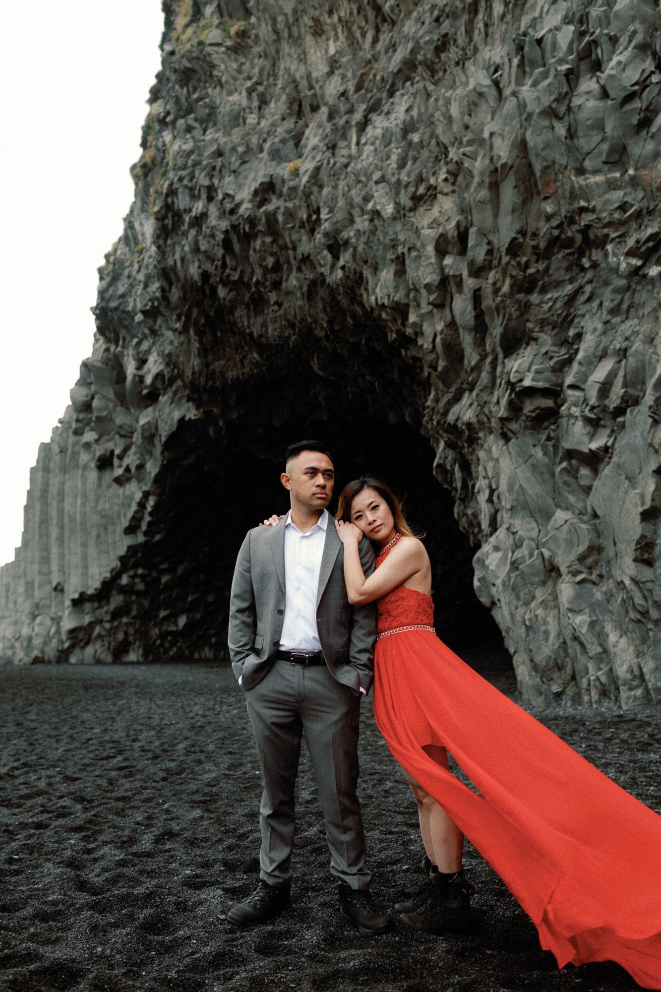 Couple posing in front of dramatic black basalt rock cave on Reynisfjara black sand beach Iceland.