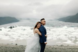 Couple in wedding attire embracing on a rocky shore with glaciers and icebergs in the background in Iceland.