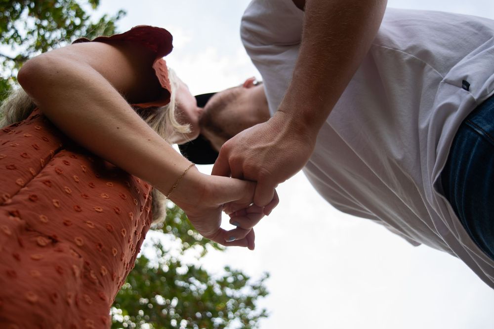 Couple holding pinkies and kissing under trees