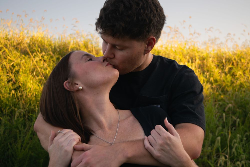 Couple hugging each other and kissing in front of a field at sunset