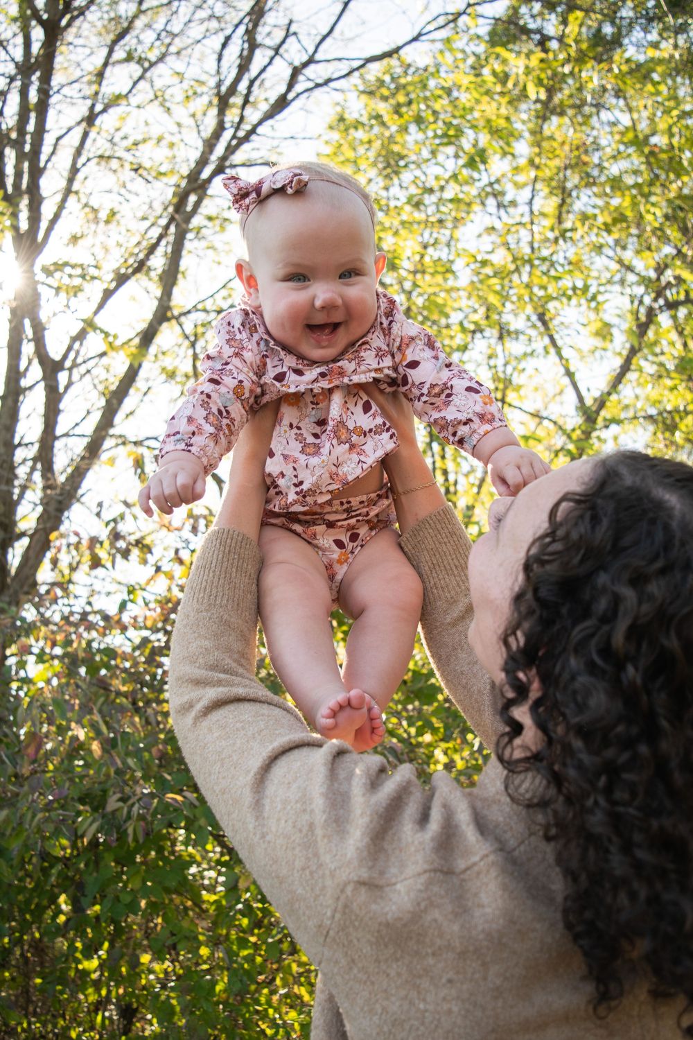 A mom holding her baby above her head and her baby is laughing