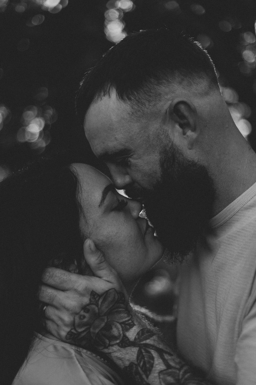 Intimate black and white portrait of couple sharing tender moment with bokeh background lighting effects.