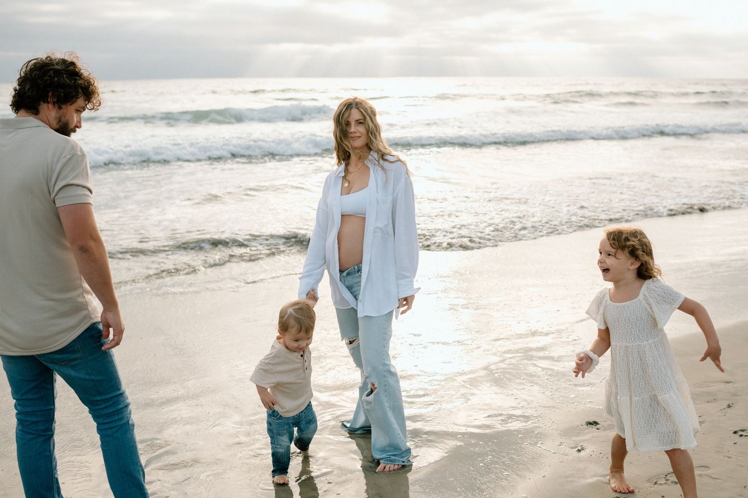 A family enjoying a sunny day together walking along the shoreline of a beach during sunset.