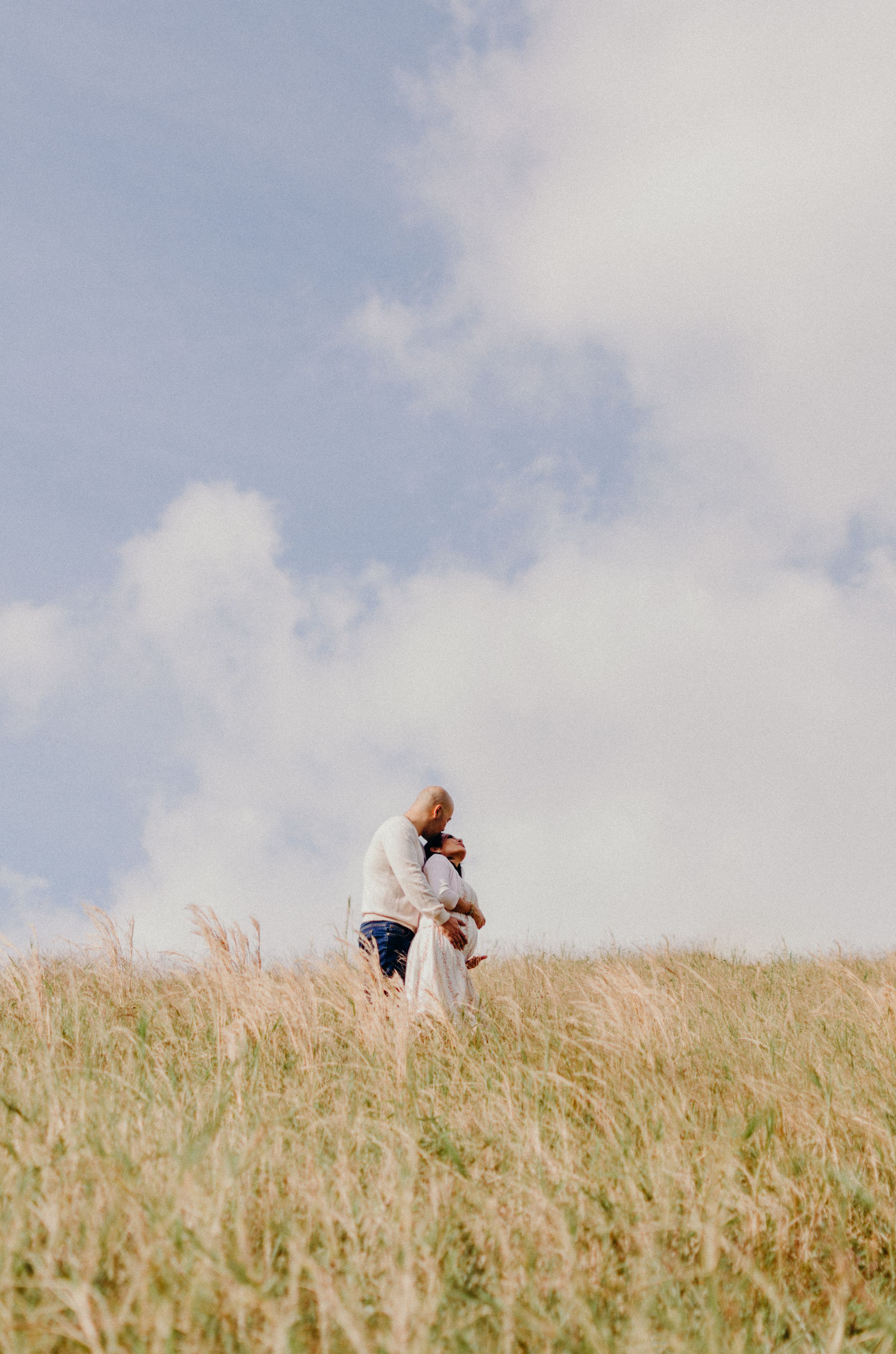 Distant silhouette of embrace in golden wheat field against cloudy sky.