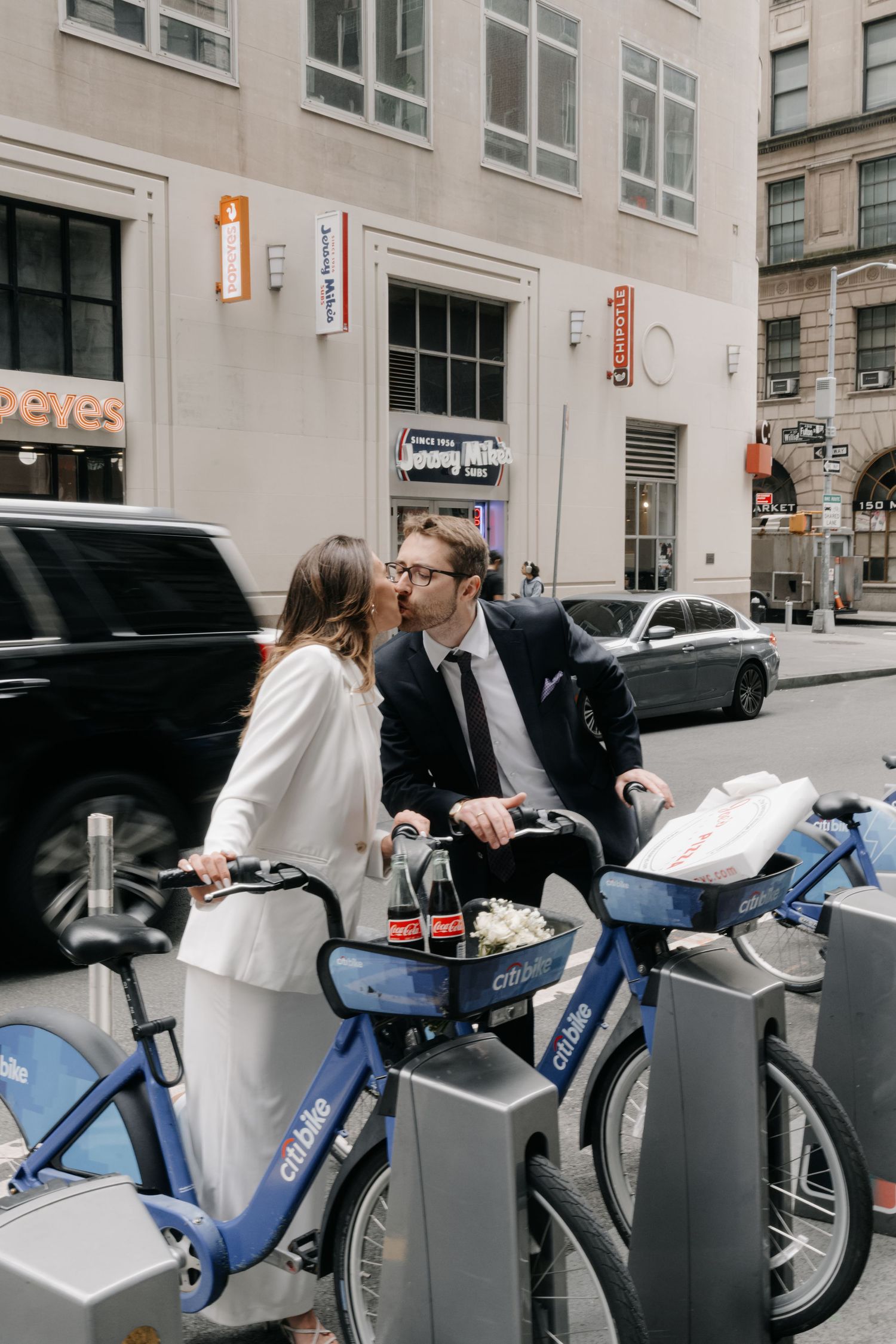 A couple renting city bikes from a bike share station on an urban street.