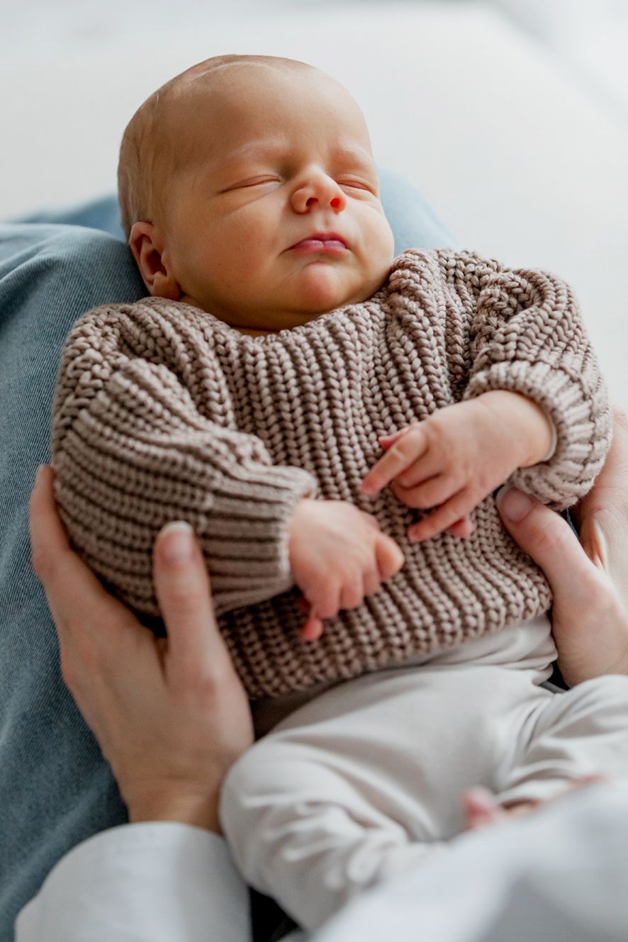 De baby ligt heel ontspannen te slapen op de knieën van mama
