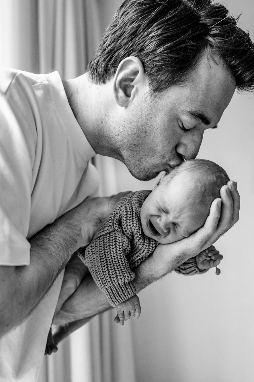 In de sterke armen van papa ligt deze kleine baby lekker te slapen tijdens de fotoshoot