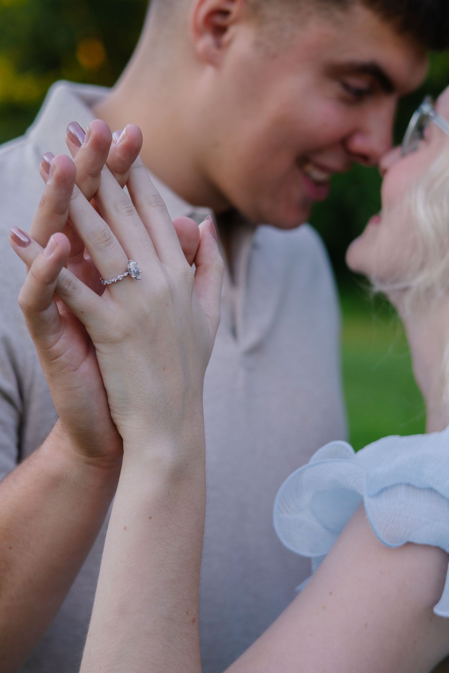 Close-up of hands holding engagement ring in outdoor setting.