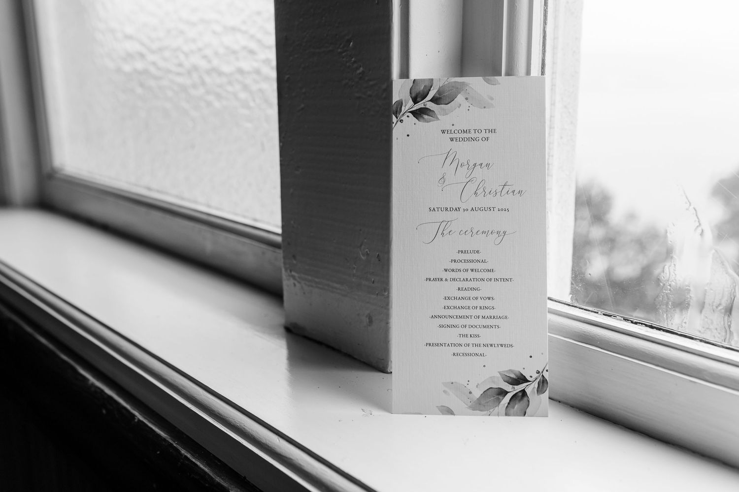 A series of black and white photographs and paper documents laid out on a windowsill in soft natural light.