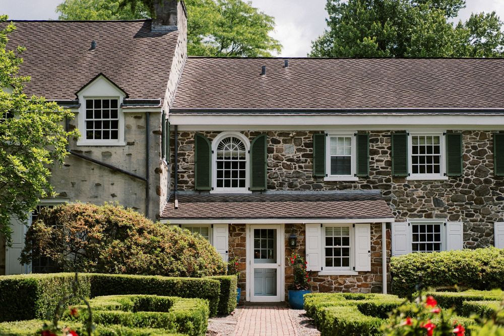 Beautiful stone mansion with traditional landscaping and elegant curved driveway surrounded by mature trees and shrubs.