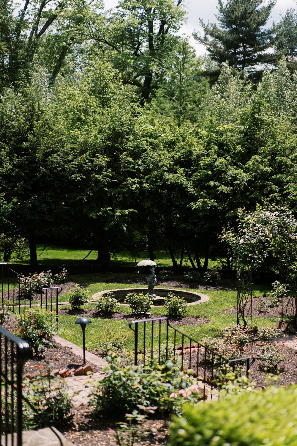Tranquil garden setting with decorative iron fencing surrounding a circular water feature and flowering plants.
