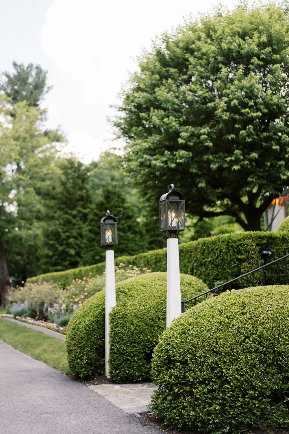 Manicured boxwood hedges line a garden path with decorative lamp posts.