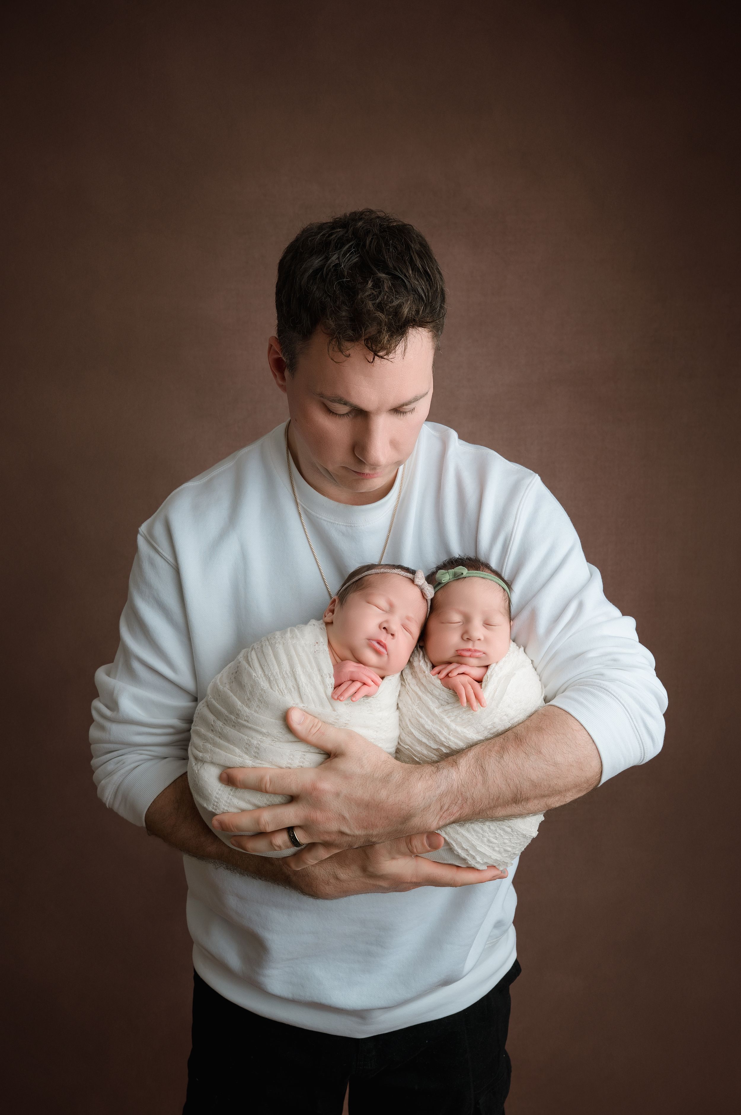 Multiple images show a person in a white sweater holding and cradling two small newborn babies against a dark background.