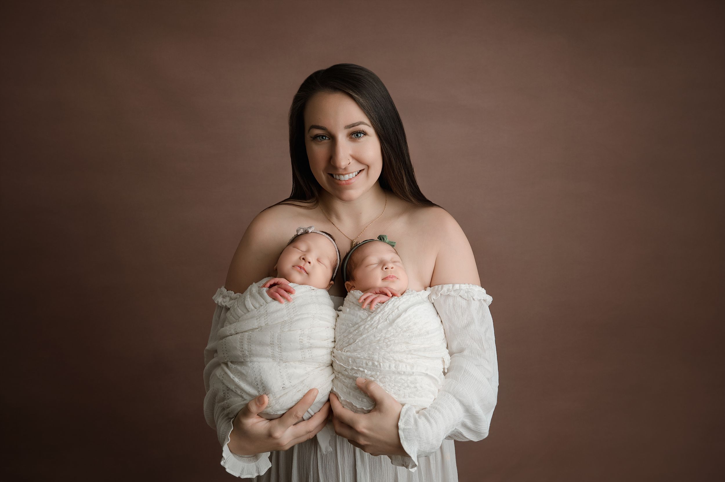 Heartwarming series of twin newborn baby portraits in white swaddles against dark brown backdrop.