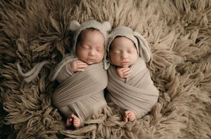 Two sleeping infants swaddled in soft beige fabric lying together on plush furry blanket.
