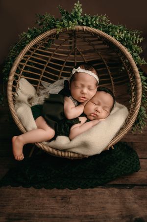 A peaceful newborn baby sleeps soundly in a cozy brown wicker basket surrounded by greenery on a rustic wooden surface.