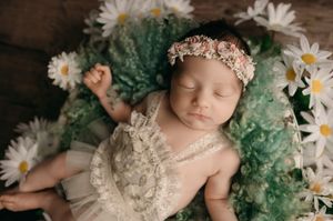 Newborn baby nestled among white daisies and mint green fabric in artistic professional photography setup.