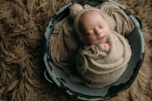Series of seven professional newborn photography portraits showing a sleeping baby wrapped in beige knit fabric on dark plates.