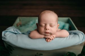 A sleeping infant rests peacefully on soft aqua-colored blankets in a professional newborn photography setting.