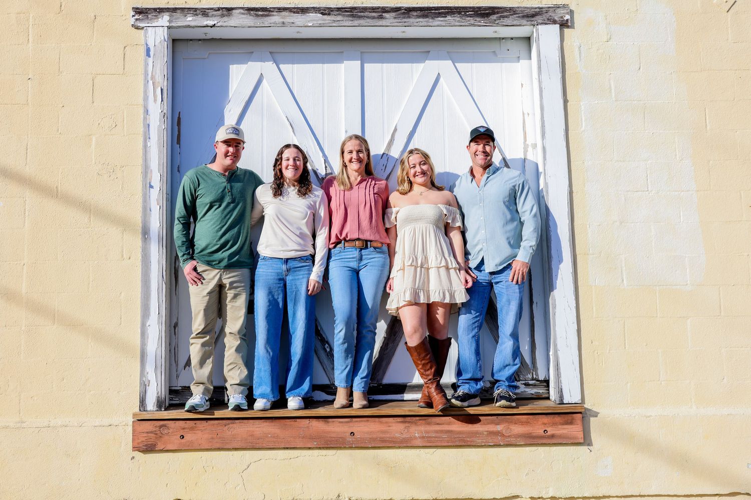 Group of people standing together in window frame against white painted building exterior.