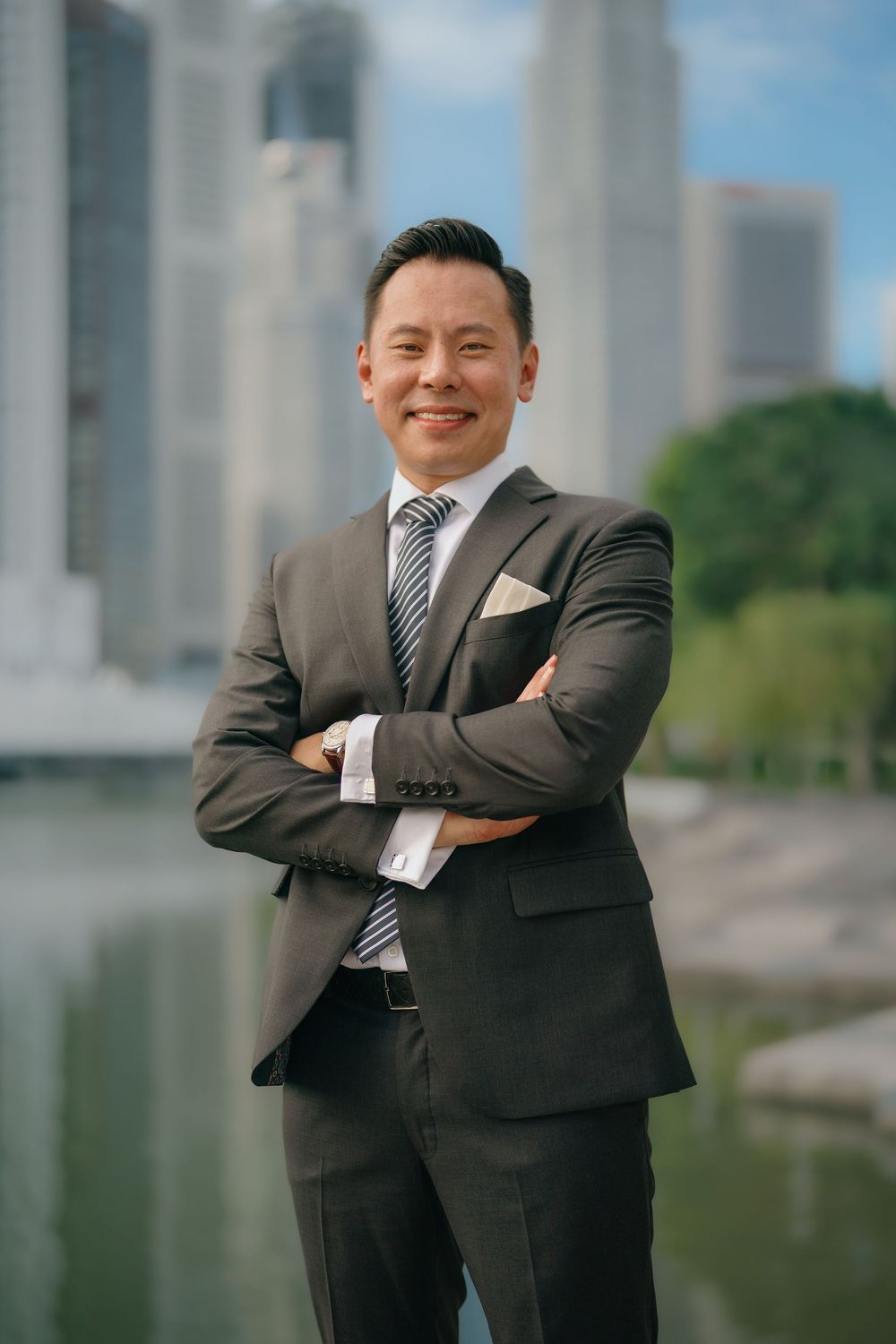 Professional portrait of a businessperson in a dark suit and tie standing confidently in front of an urban background.