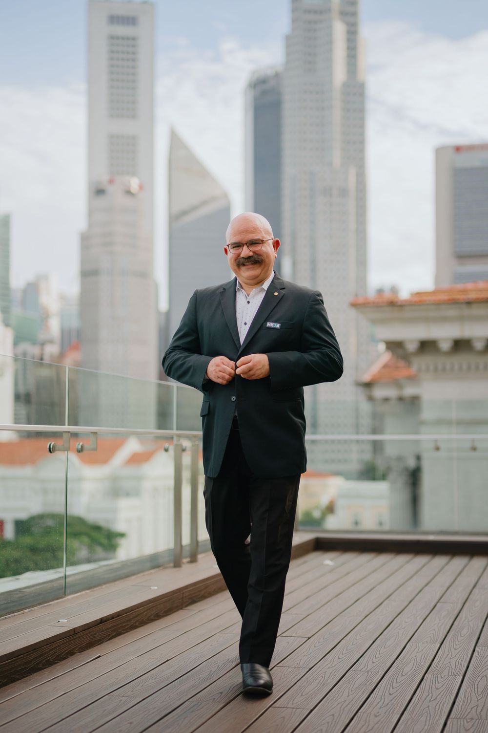 Professional in a black suit posing in front of Singapore's modern cityscape on a rooftop terrace.