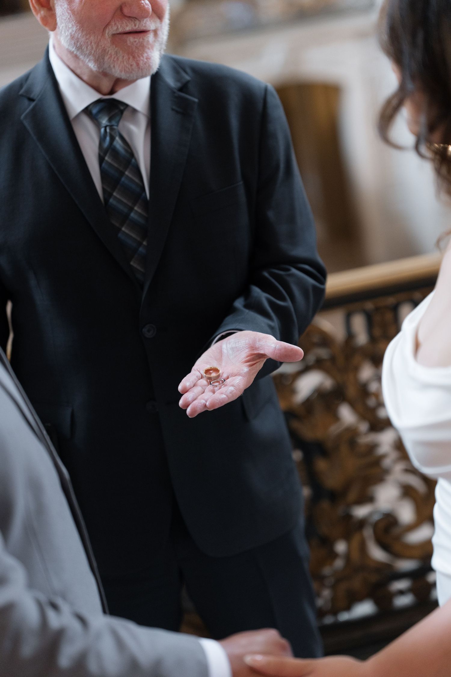 Elderly person in business suit making an expressive hand gesture while speaking in a formal setting.