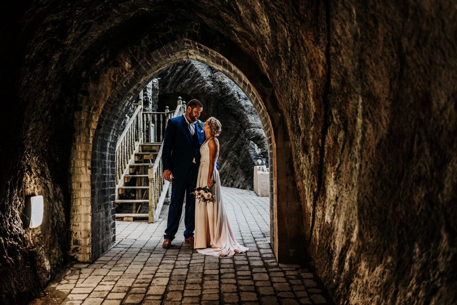 Romantic wedding portrait in stone tunnel with natural lighting and archways.