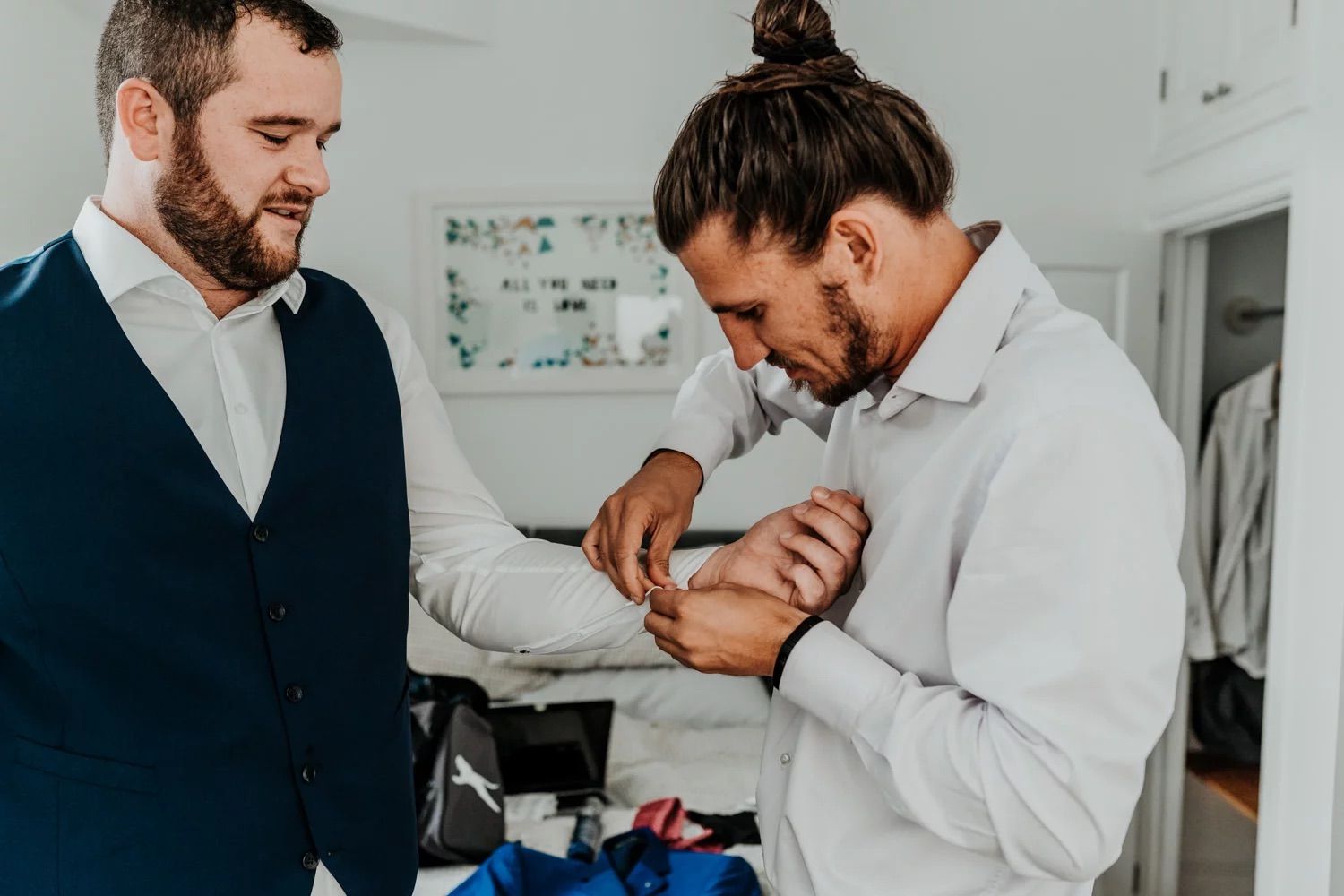 Wedding preparation moments as men help each other get dressed in crisp formal attire.