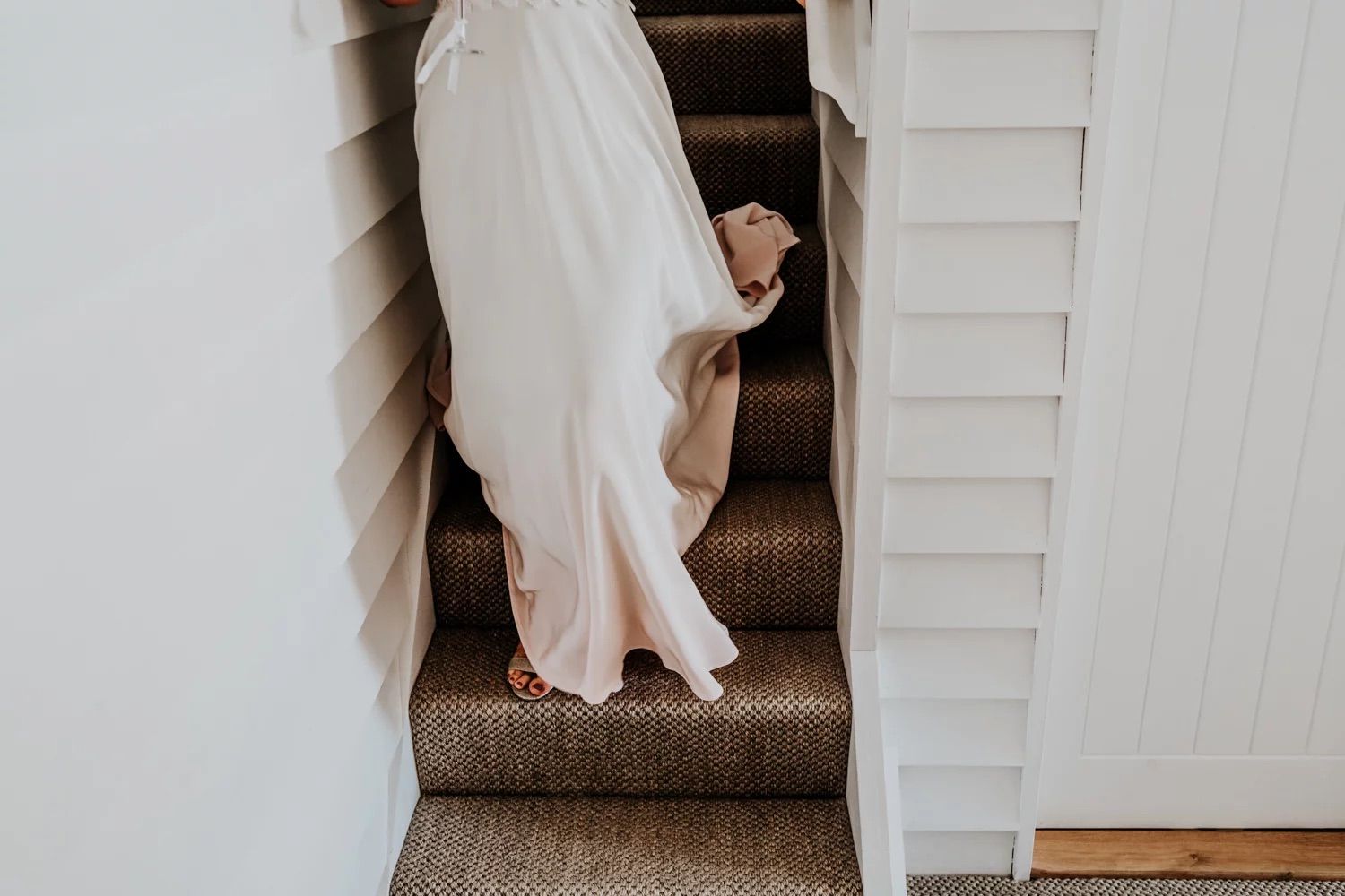 Long flowing white train of a wedding dress cascading down wooden stairs in an intimate indoor setting.