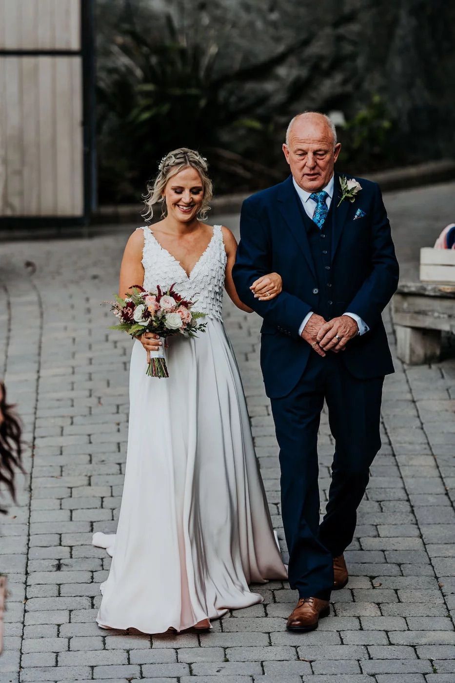 Wedding couple walking down a cobblestone path wearing white dress and navy suit.