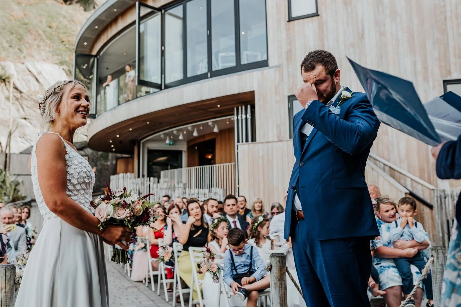 Wedding ceremony in a modern venue with large windows and guests seated in rows.