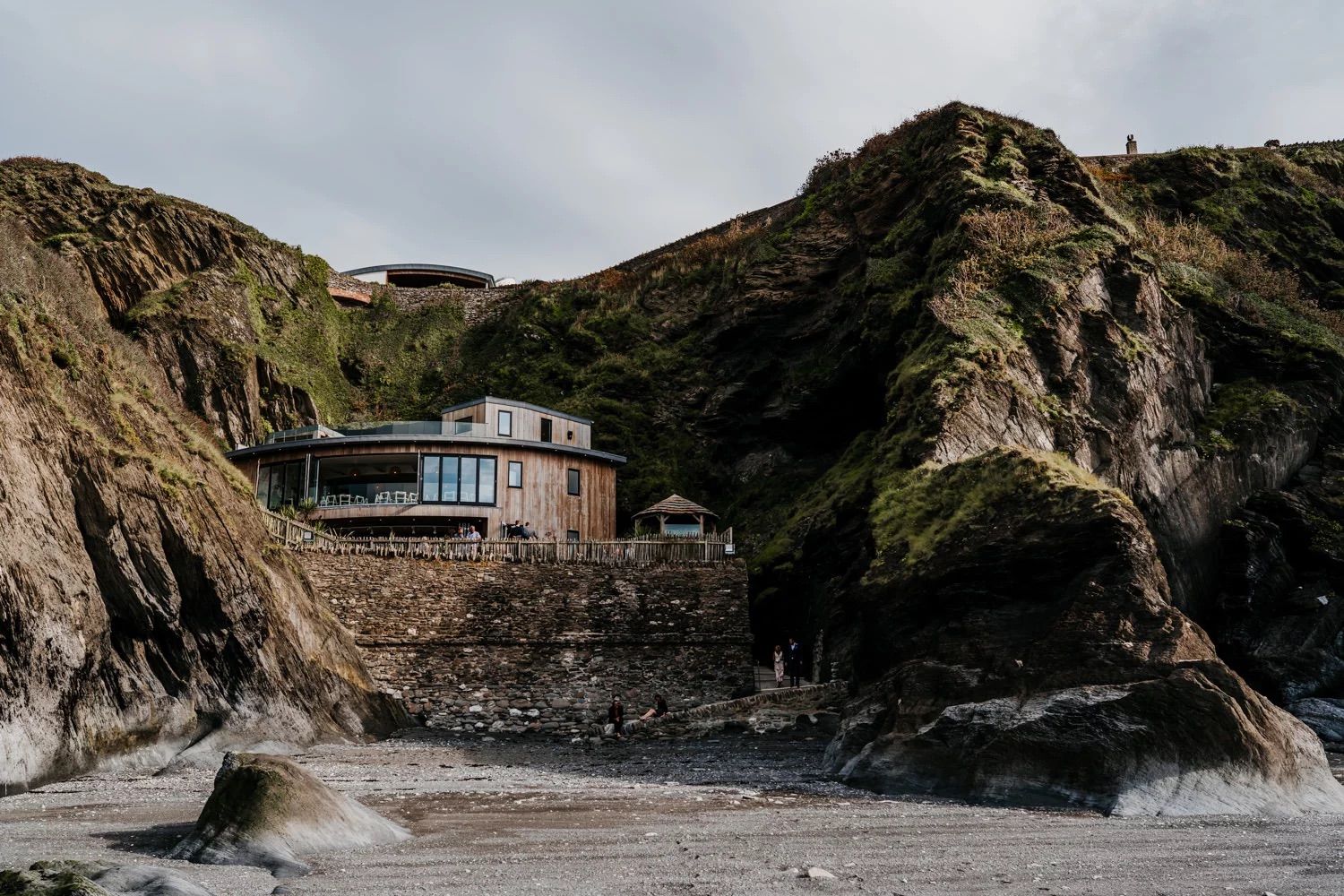 Dramatic aerial view of a rocky coastline with cliffside buildings and crashing waves below.