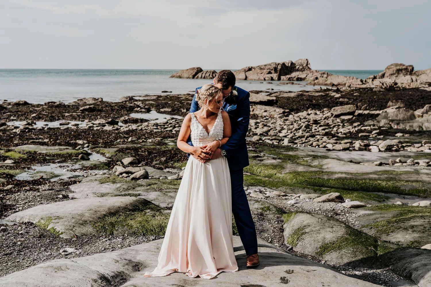 Couple walking along rocky coastal shoreline during sunset photoshoot.