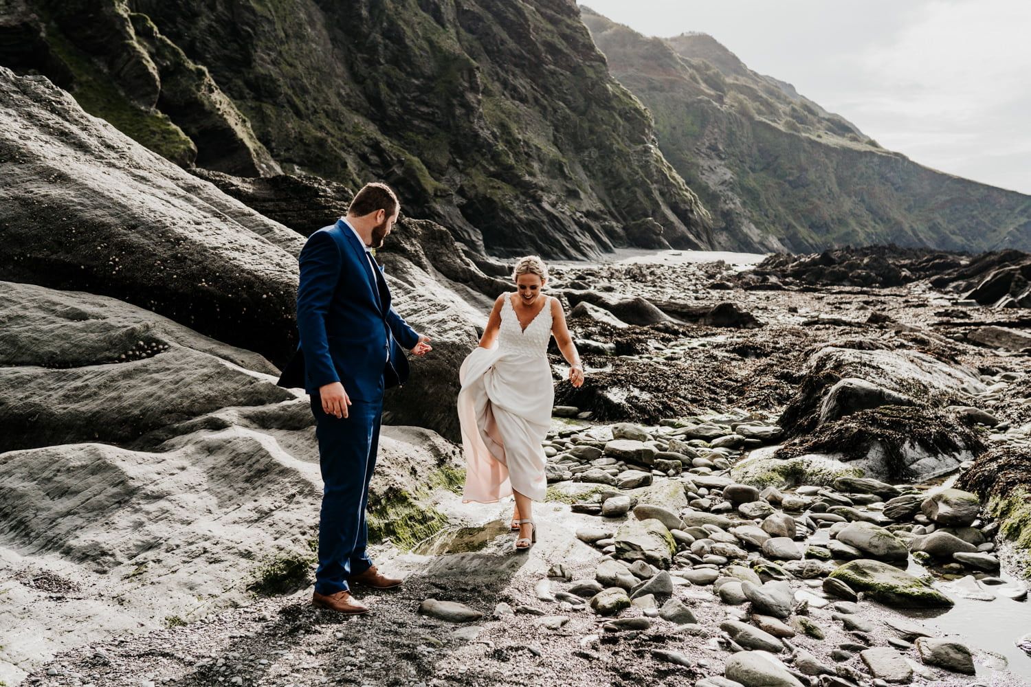 Couple walking along dramatic rocky coastline during wedding photoshoot.