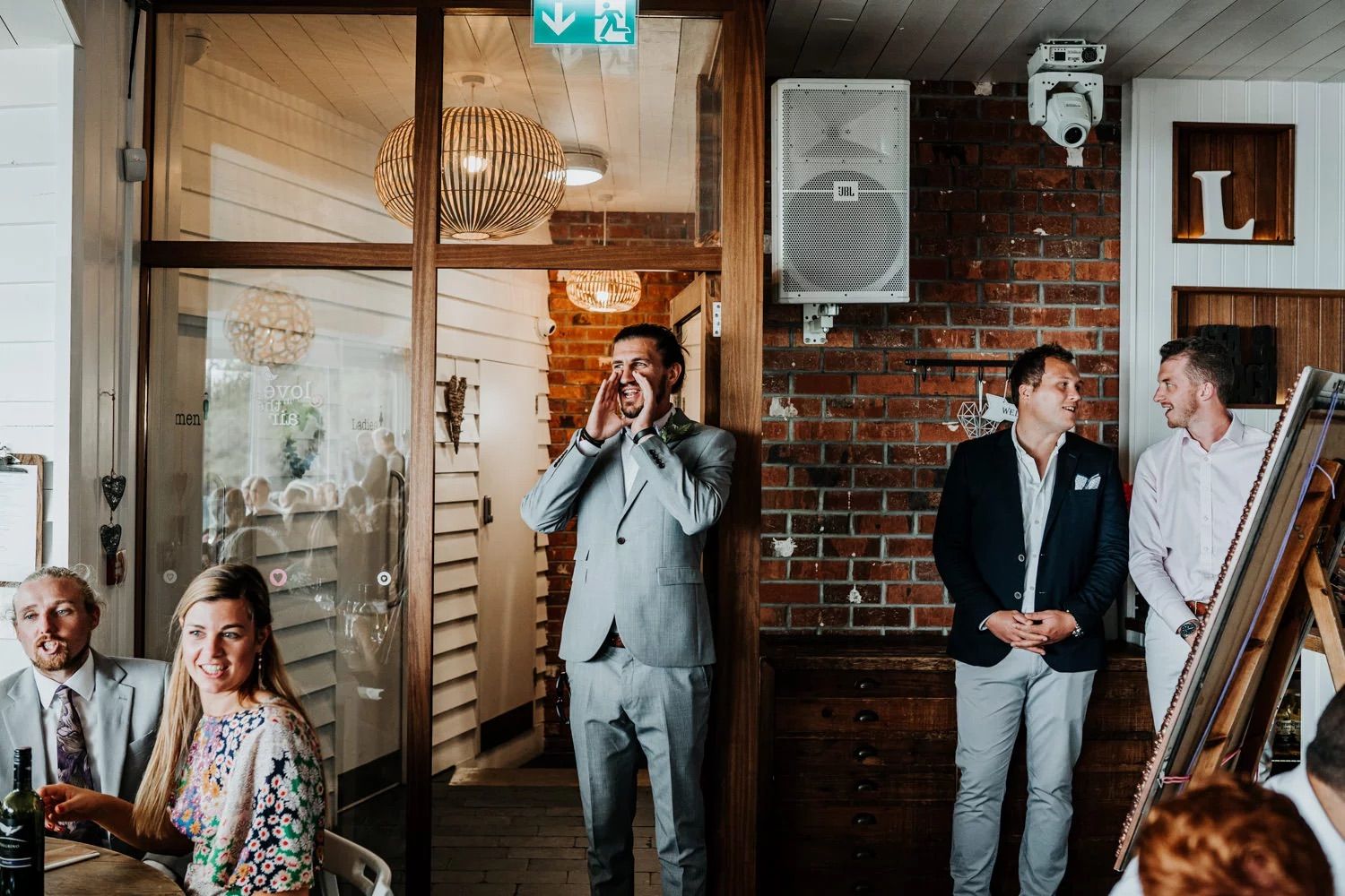 Wedding party mingles in a rustic brick-walled venue during reception celebrations.