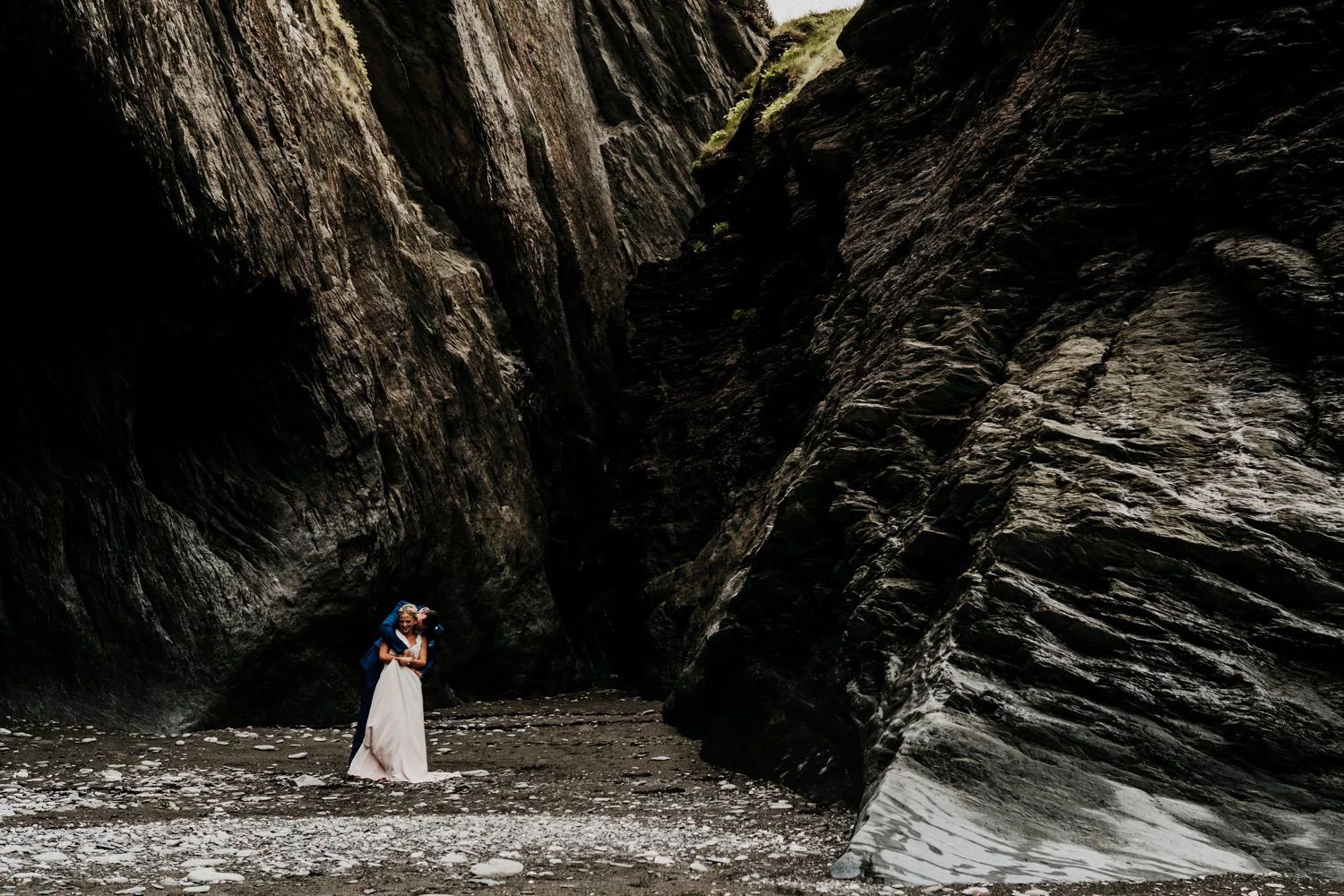 Dramatic coastal wedding photos with dark rocky cliffs and ocean waves in the background.