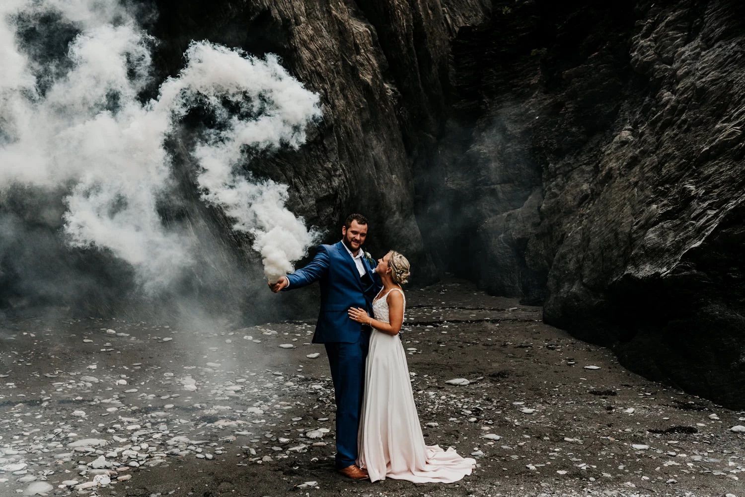 A romantic couple poses together near dramatic black cliffs and moody storm clouds during their photoshoot.