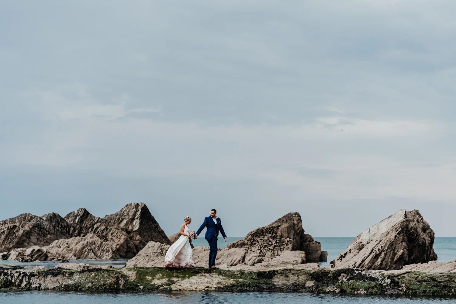 A picturesque series of coastal rock formations line the ocean shore under cloudy skies.