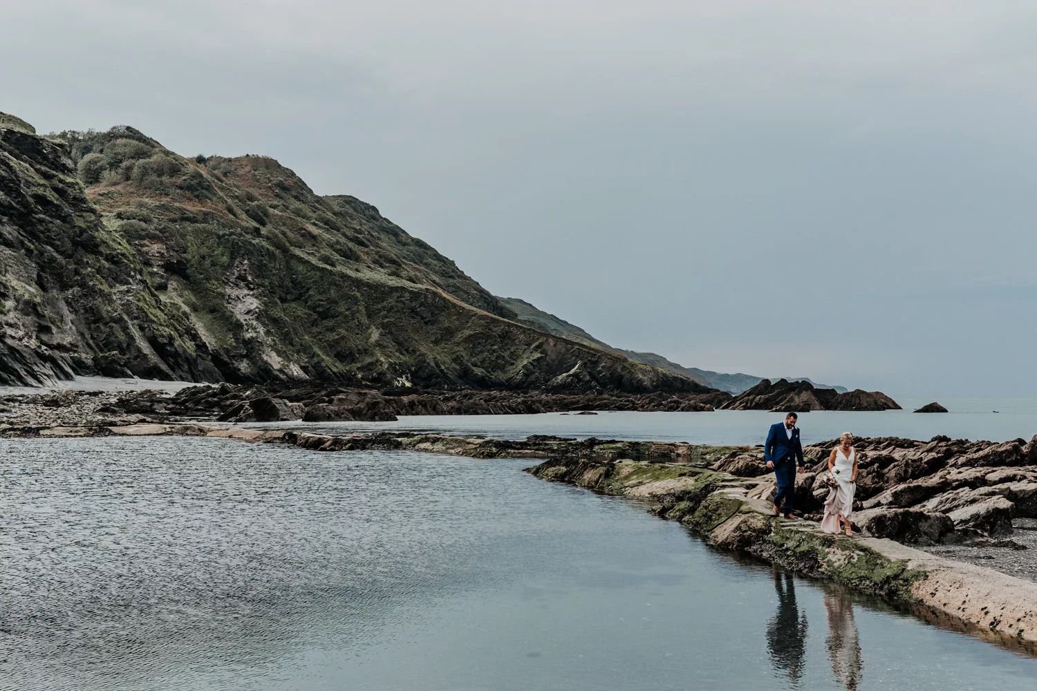 Scenic coastal landscape with rocky cliffs and calm waters under an overcast sky.