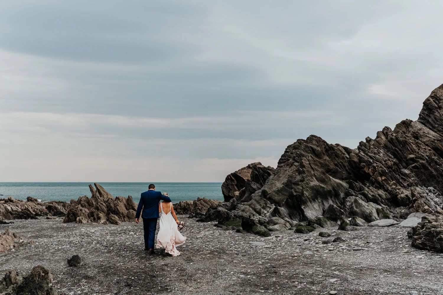 Dramatic coastal wedding photography with rocky cliffs and ocean backdrop.