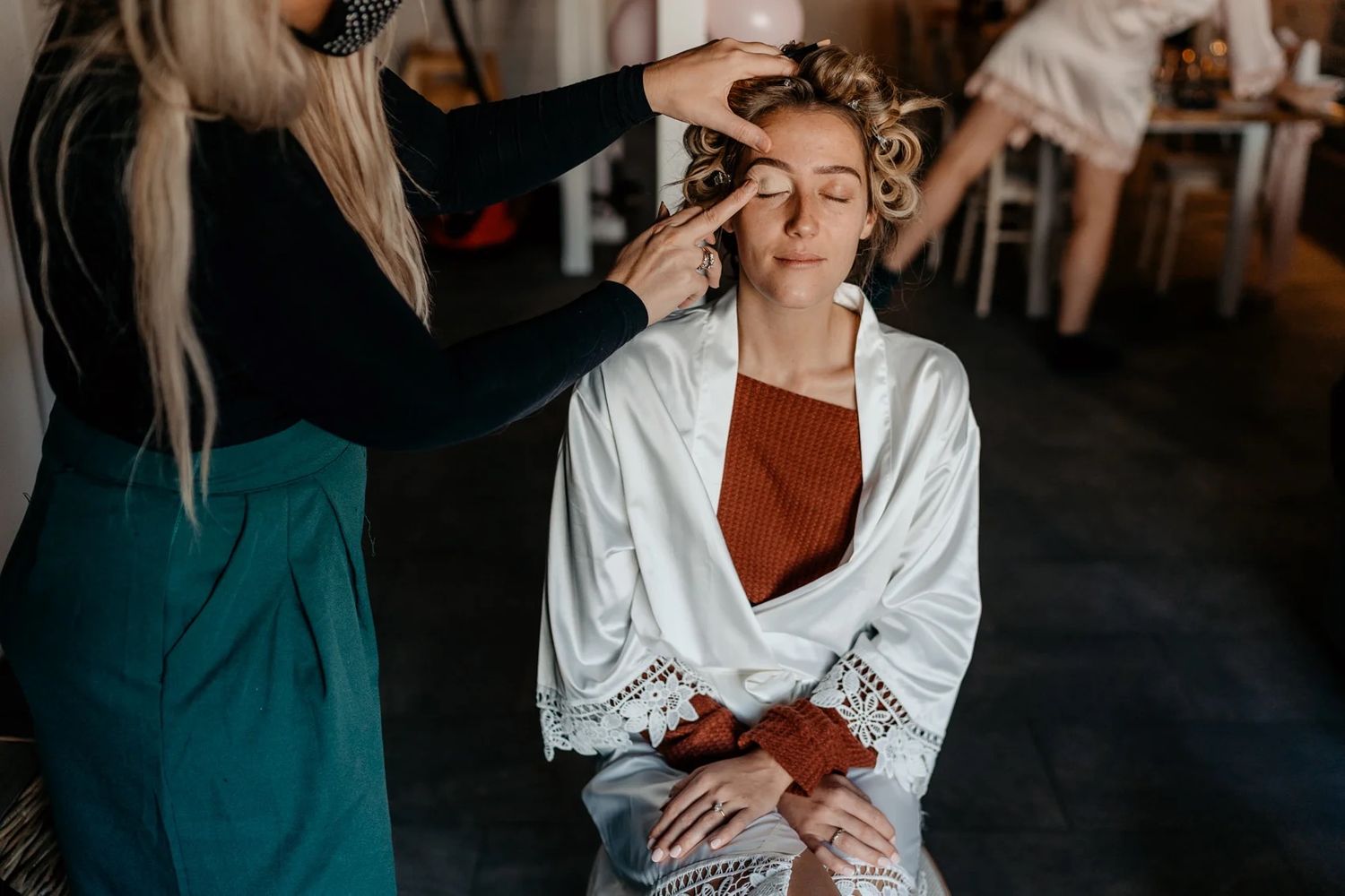 Makeup artist applies cosmetics to someone wearing a white robe during a beauty preparation session.