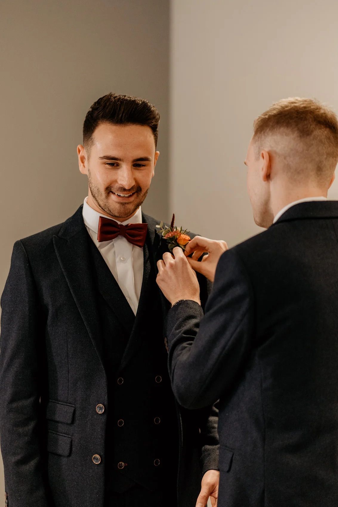 Groom and groomsmen share emotional reactions while getting ready in formal attire.