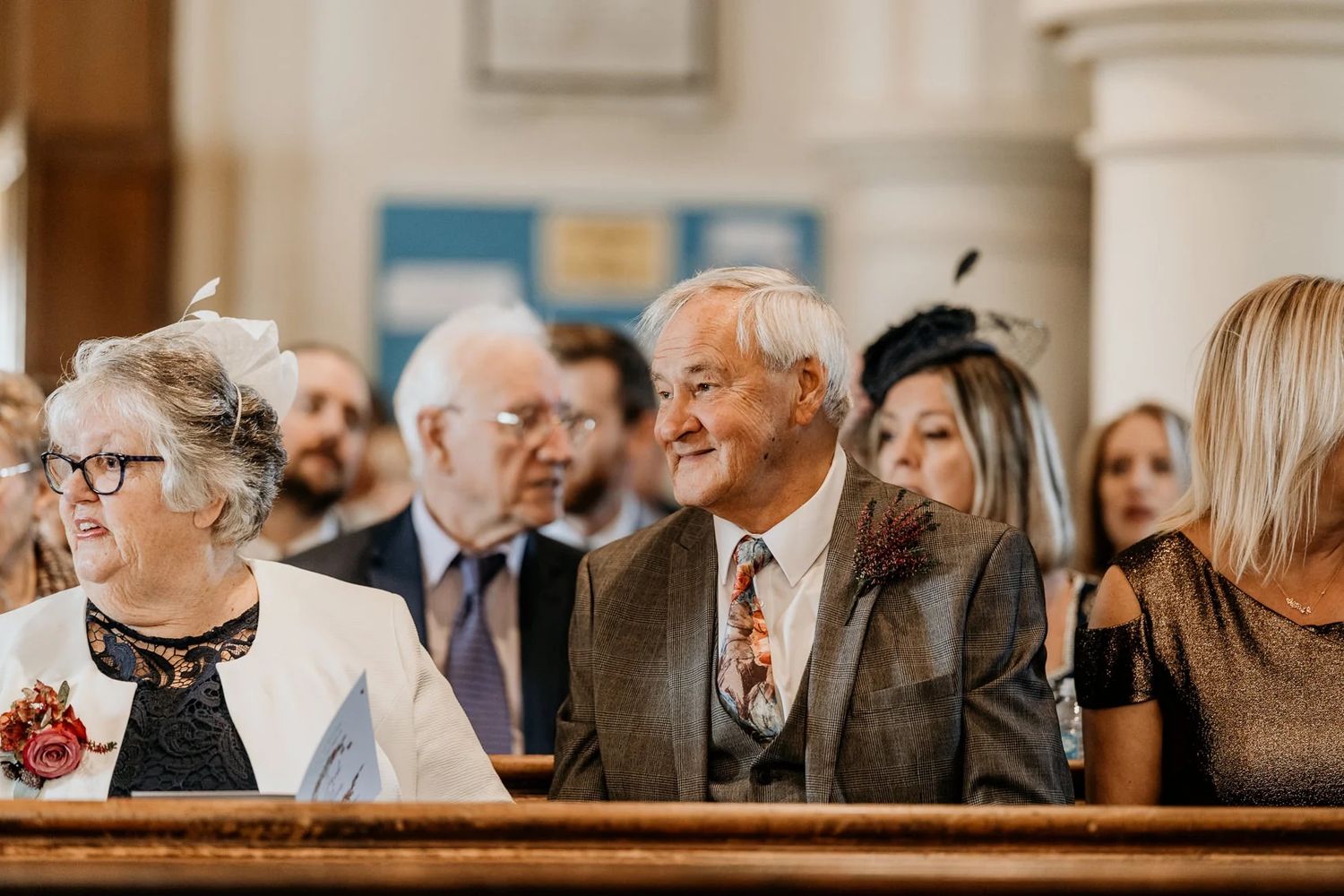 A crowd of wedding guests sit in church pews during a ceremony.