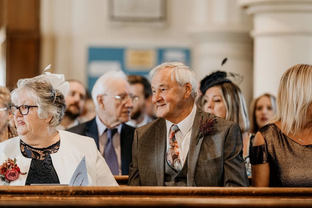 A crowd of wedding guests sit in church pews during a ceremony.