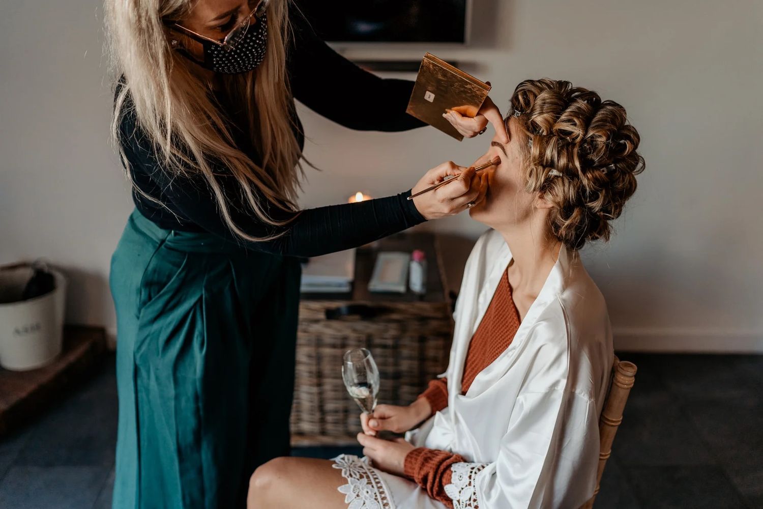 Professional stylist works on hair and makeup during a beauty session in a dimly lit room.