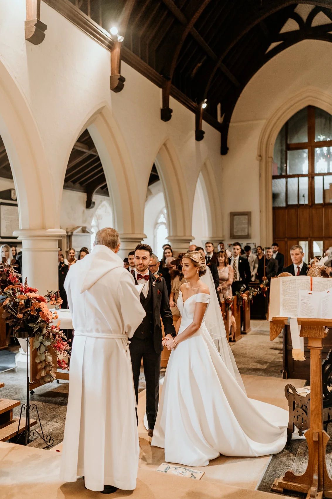 Traditional church wedding ceremony with white arches and wooden beams in a beautiful cathedral setting.